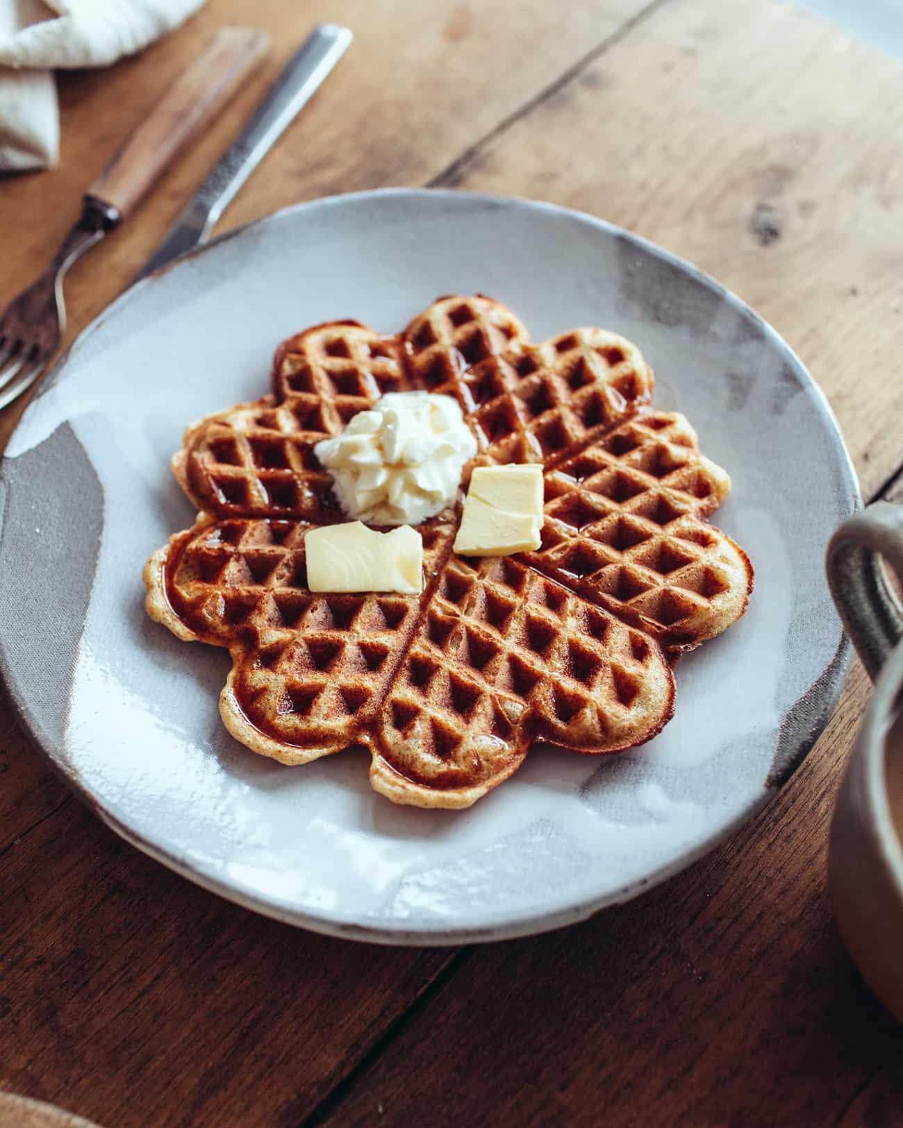 a plate with a crispy vegan waffle topped with soy cream and vegan butter