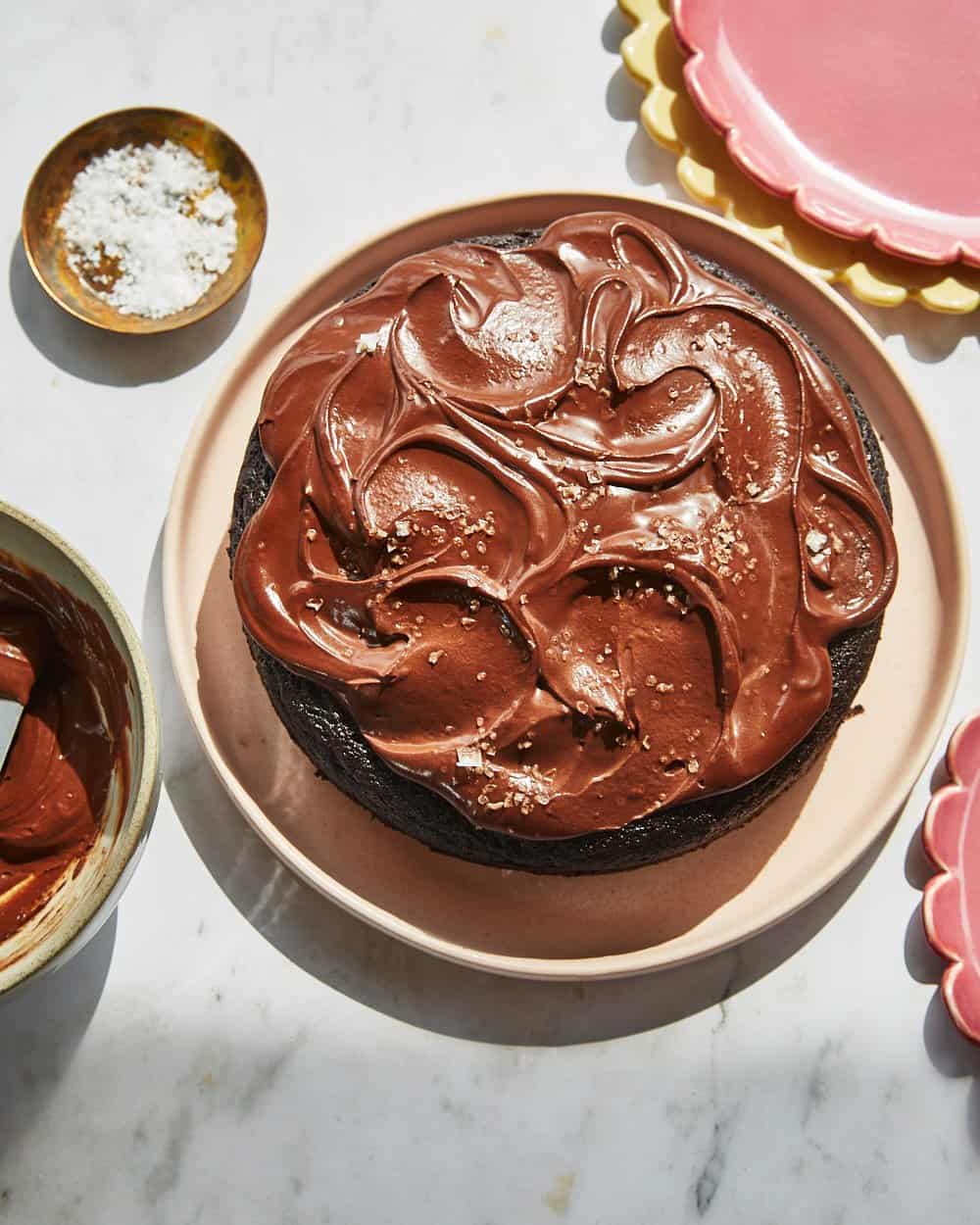 a single layer, easy chocolate cake with swirly chocolate frosting on a plate with cake plates to the side