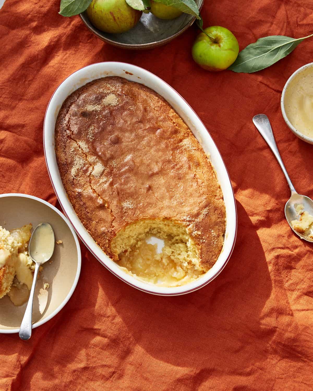 Eve's pudding in an oval dish with a scoop taken, apples in background