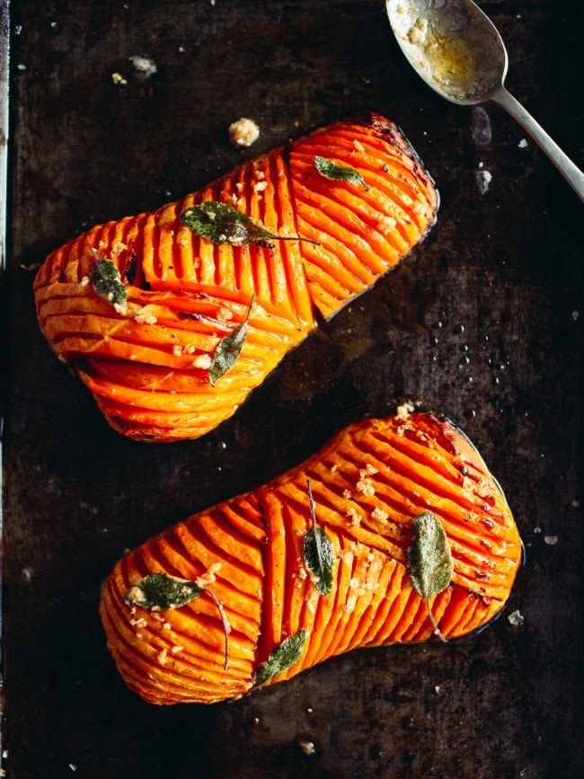 a baking tray with halved roasted butternut squash with decorative slits cut covered with garlic sage butter