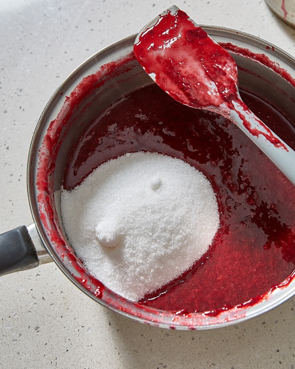 adding sugar to damson puree in a pot