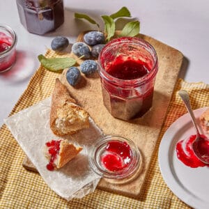 a jar of homemade damson jam with baguette and fresh damsons