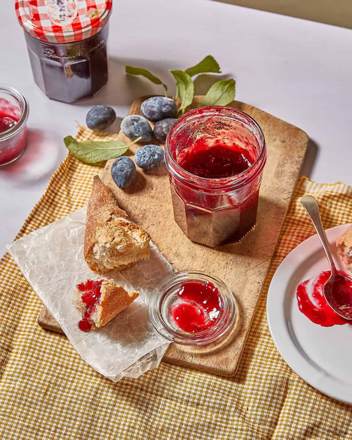 a jar of homemade damson jam with baguette and fresh damsons