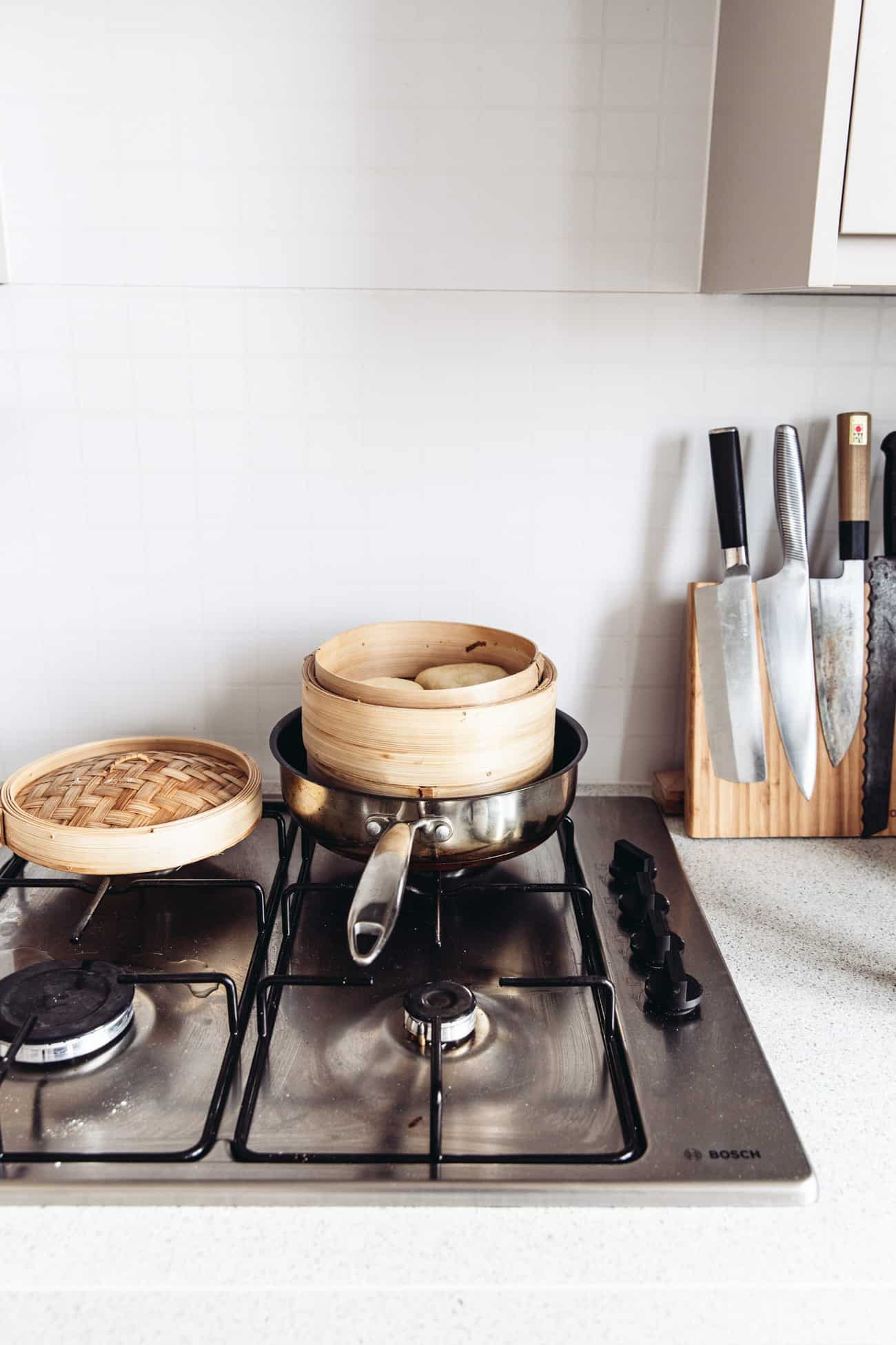 A bamboo steamer with bao buns in a pan on the stove