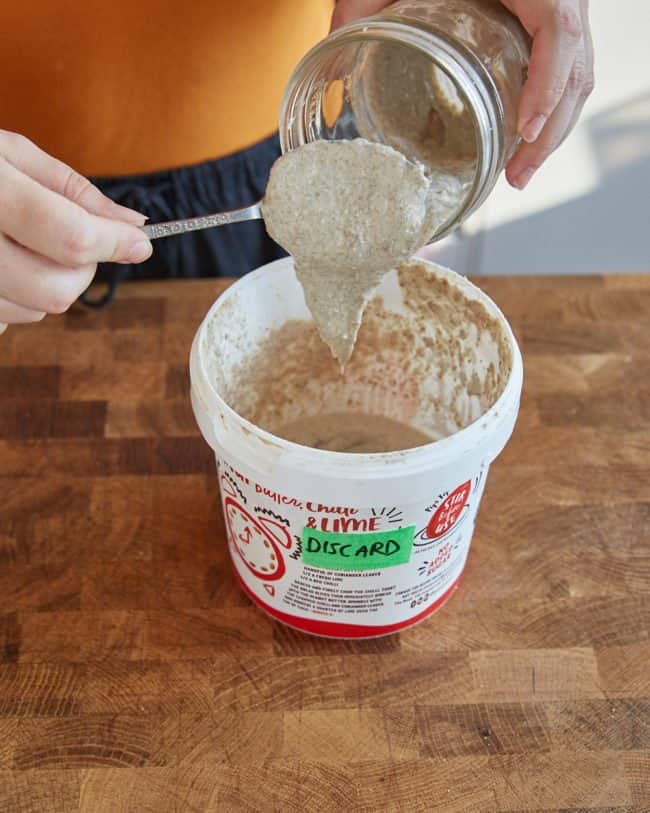 scraping sourdough starter into a tub labelled discard