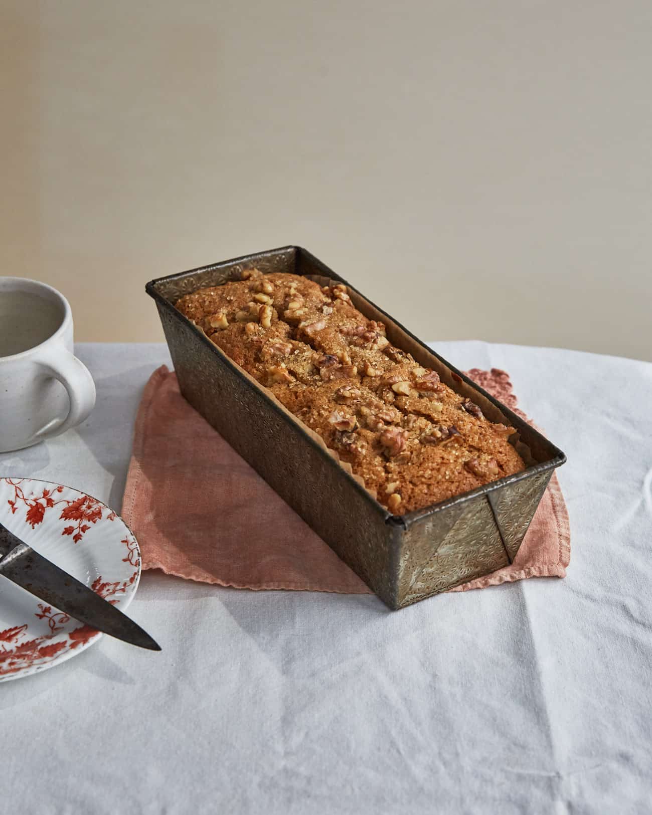 eggless banana bread in loaf tin with plate and mug