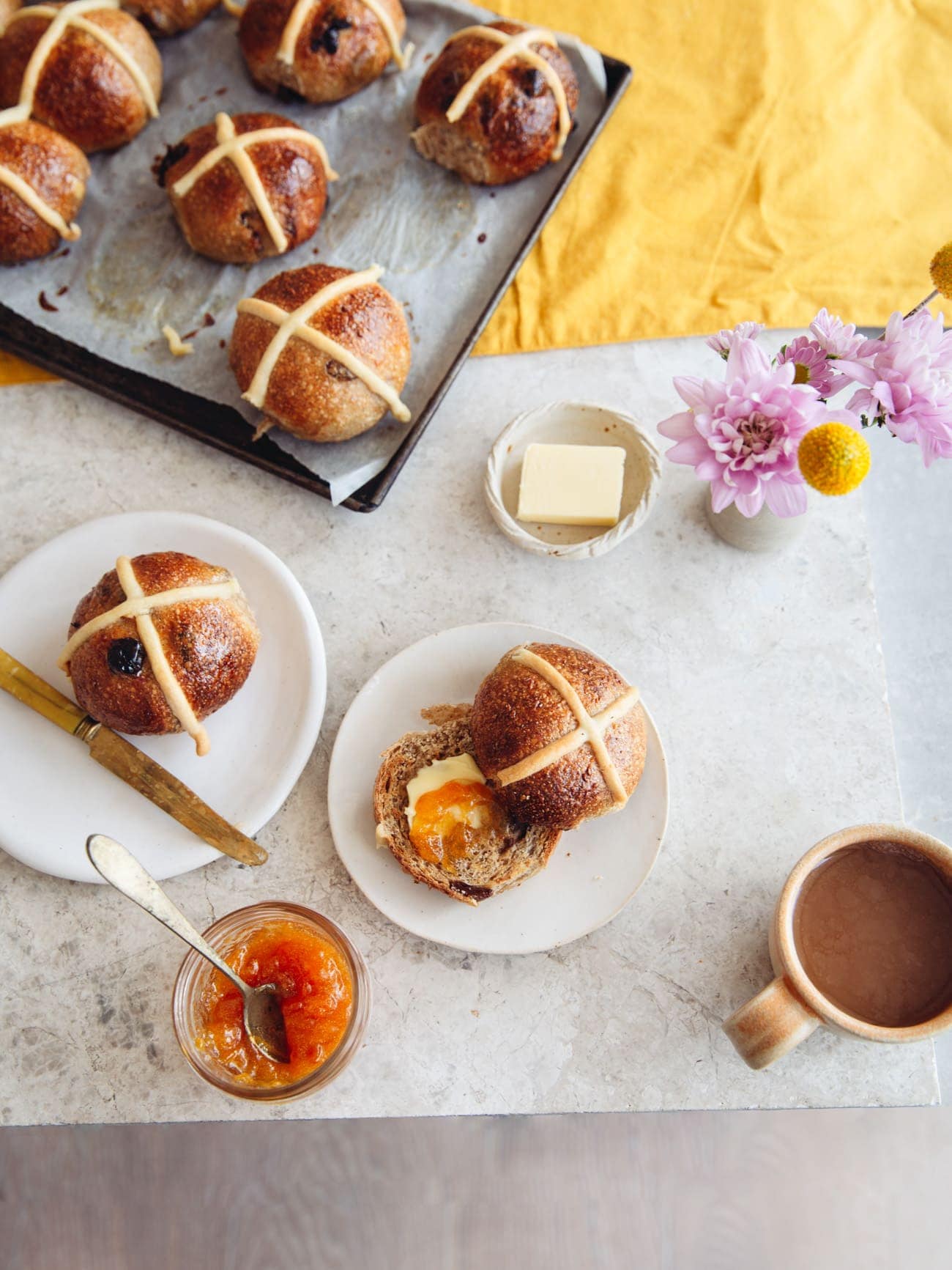 Sourdough Hot Cross Buns on a table with butter and jam by Izy Hossack