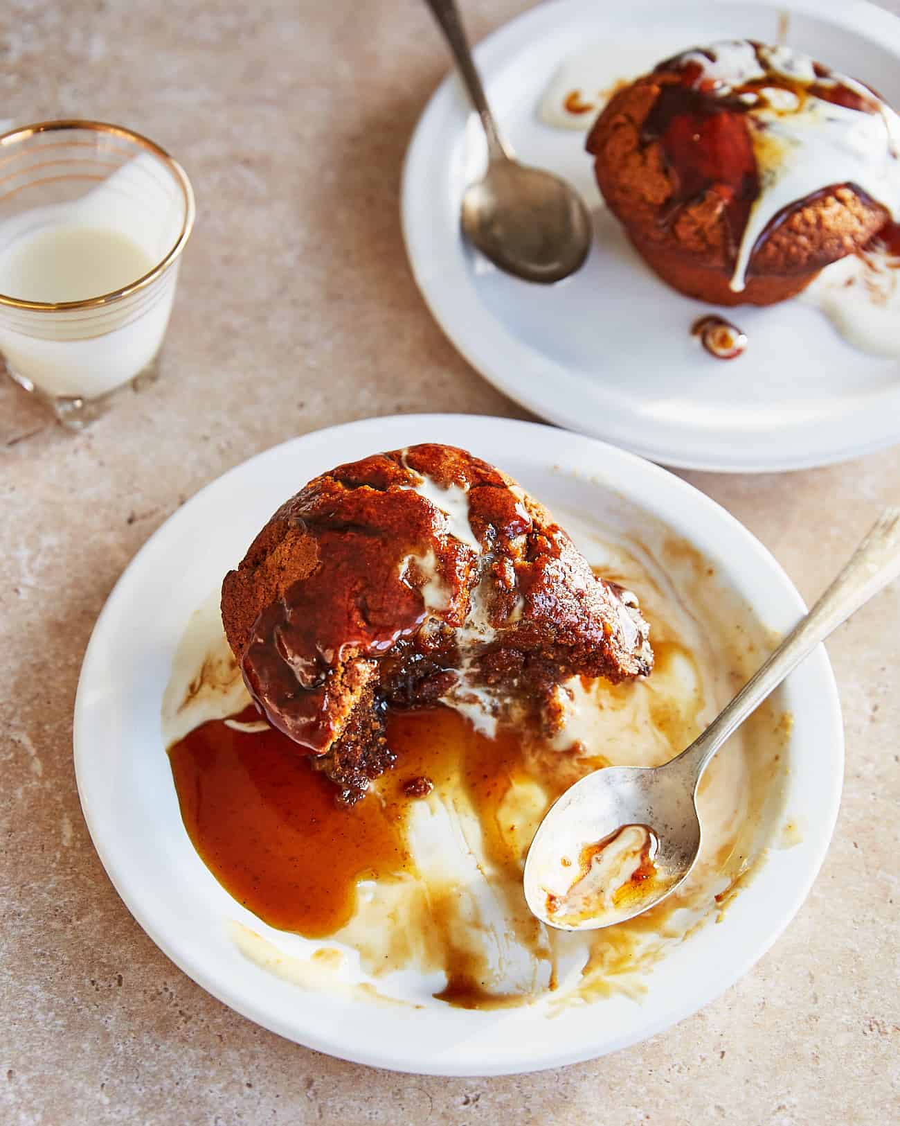 two servings of sticky toffee pudding with toffee sauce and soy cream with a bite taken.