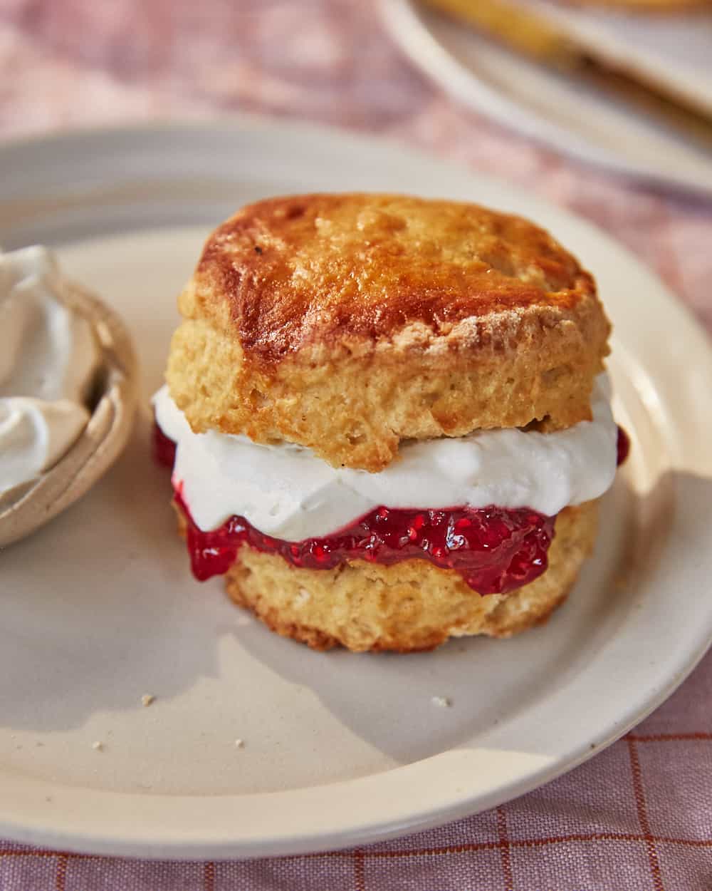 a vegan scone split in half with whipped oat cream and raspberry jam on a plate