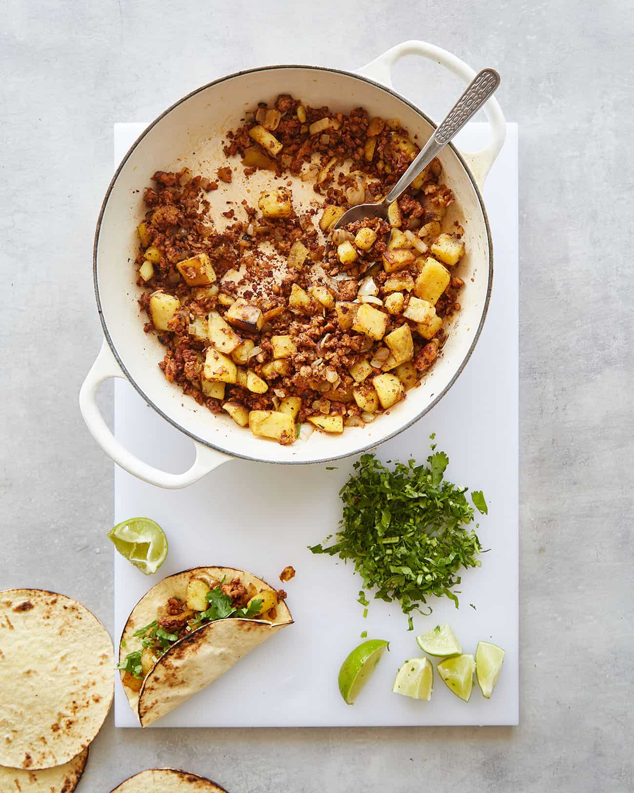 a pan of vegan chorizo potato mixture on a board with a taco, cilantro and lime